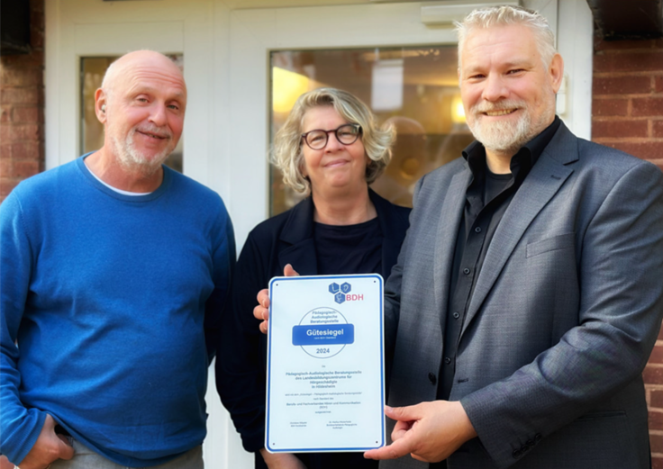 Foto zeigt ein Urkunde mit Gütesigel und drei Personen